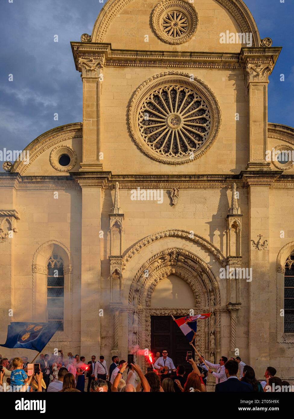 il fumo riempie l'aria dai riflessi rossi mentre una festa di nozze celebra il sole della prima sera di fronte alla cattedrale di sibenik Foto Stock
