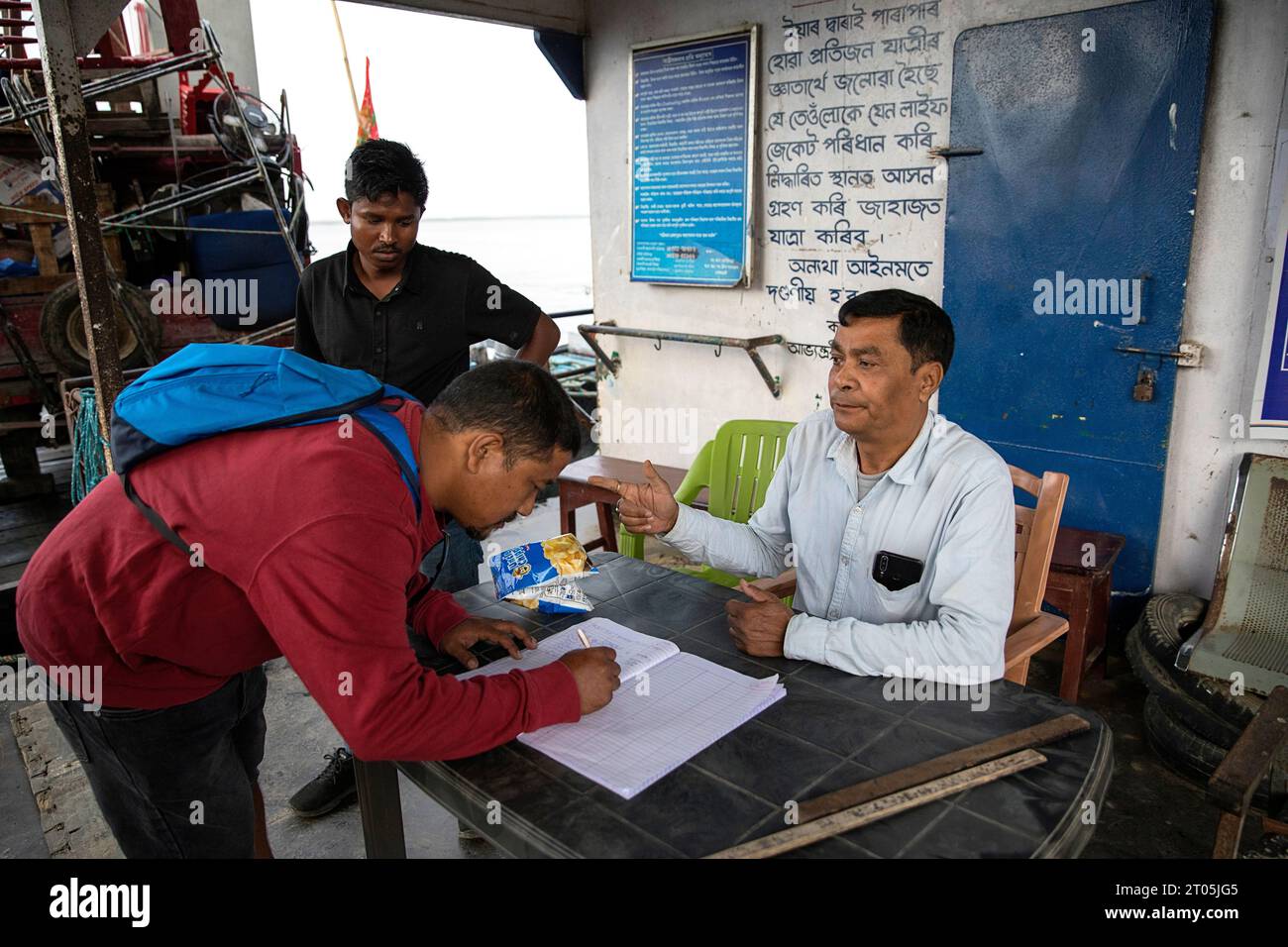 Gente del posto, passeggeri che firmano un libro prima di imbarcarsi in un viaggio in traghetto per l'isola di Majuli, viaggiando sul fiume Brahmaputra, Assam, India Foto Stock