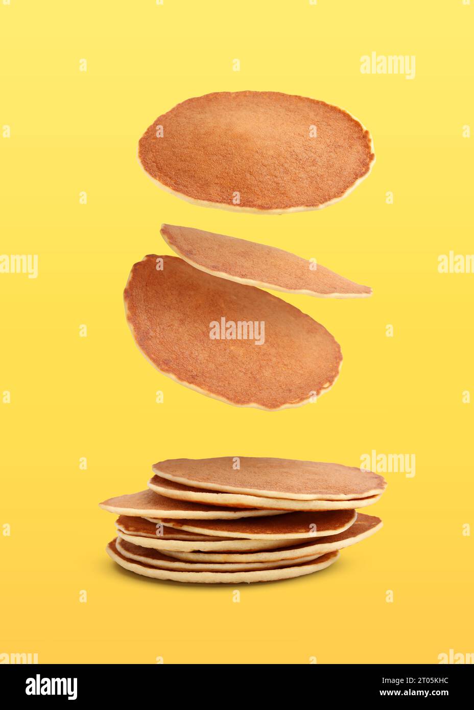 Molti gustosi pancake freschi che cadono su sfondo dorato Foto Stock