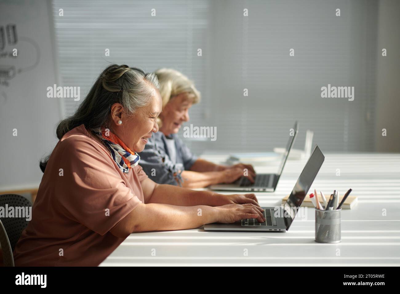 Donna anziana felice che impara a lavorare in un notebook in classe per principianti Foto Stock