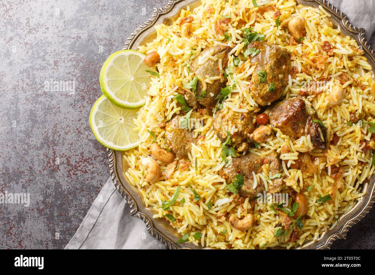 Festive pilaf Kacchi Mutton Biryani con noci, uvetta, primo piano di cipolla fritta sul piatto sul tavolo. Vista superiore orizzontale dall'alto Foto Stock