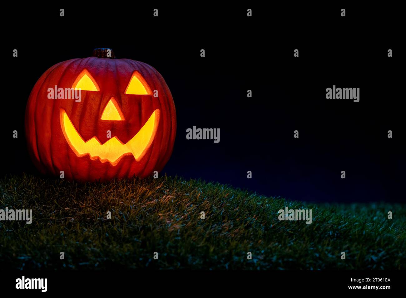 Un sorridente Jack o Lanterna seduto nell'erba come decorazione di Halloween. Si illumina dalla luce interna ed è accentuata dalla luce blu della luna. Foto Stock
