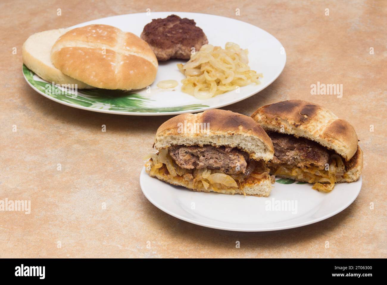 Uno split hamburger rivela la sua succosa carne su un piatto, con un pezzo di hamburger tostato, pane e cipolle dorate sullo sfondo. Cuocete la vostra OW Foto Stock