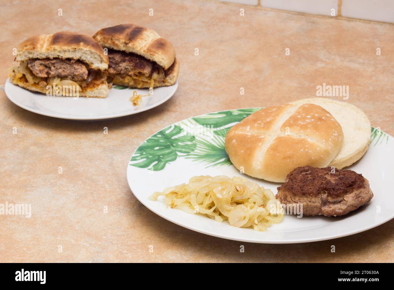 Un appetitoso hamburger tostato, pane e cipolle dorate in primo piano su un piatto. Sullo sfondo, uno split hamburger rivela il suo succoso Foto Stock