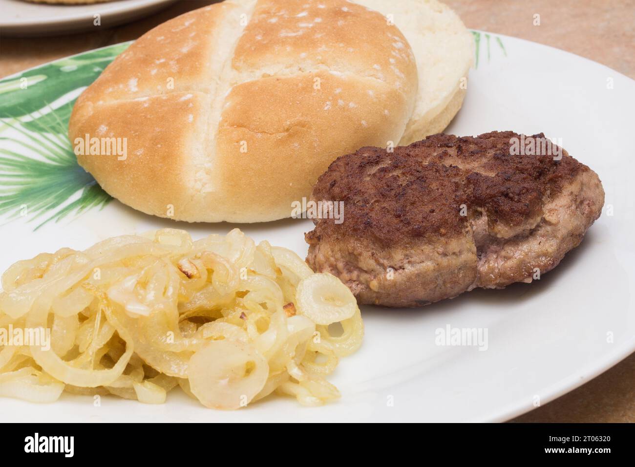 Un succulento primo piano di hamburger tostato, accompagnato da un panino hamburger e cipolle dorate traslucide su un piatto bianco. Burger Moment. Foto Stock