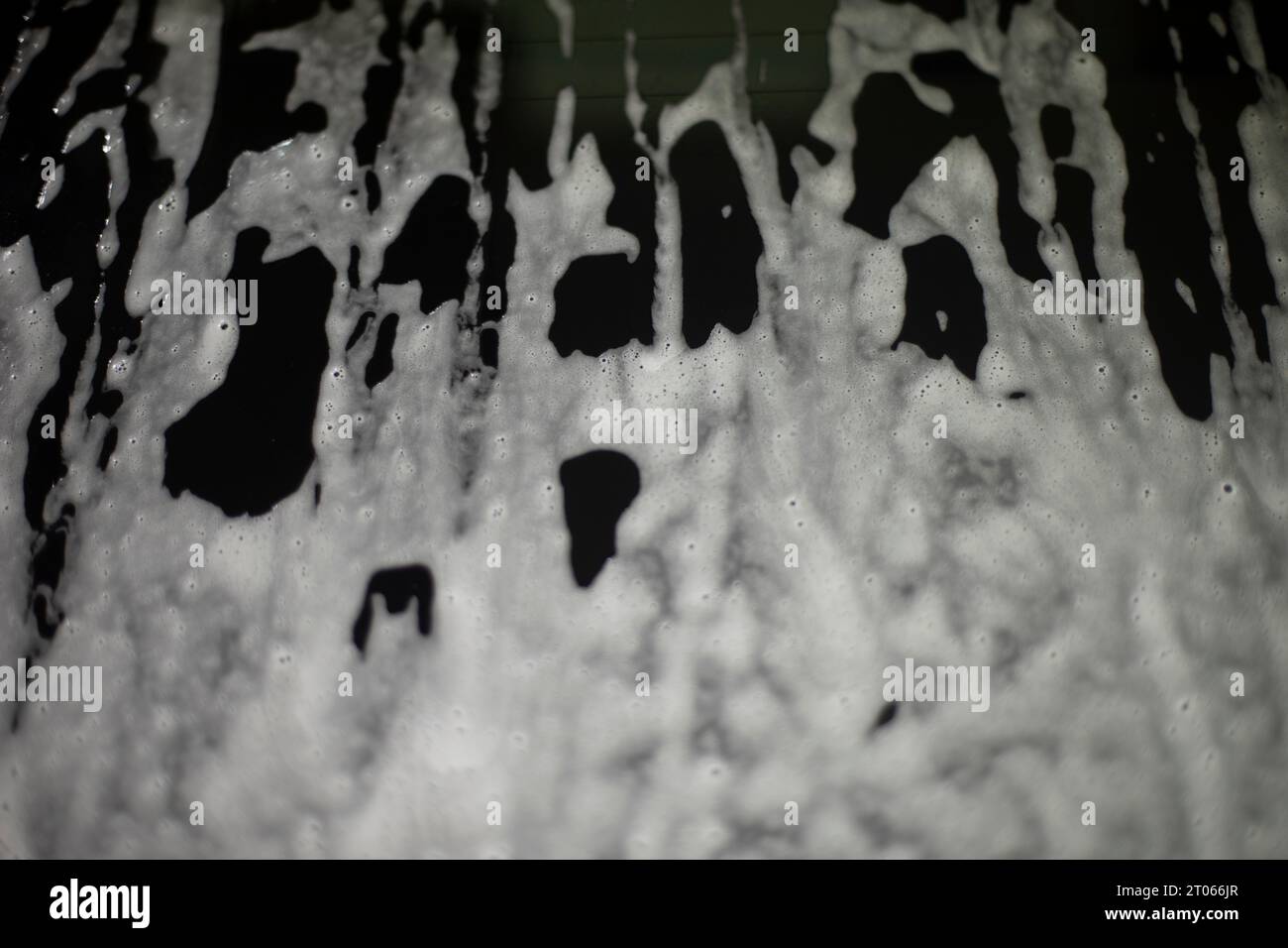 Schiuma di sapone su superficie scura. Risciacquo dello sporco dal vetro. Soluzione saponosa sull'auto. Consistenza della soluzione bianca. Foto Stock