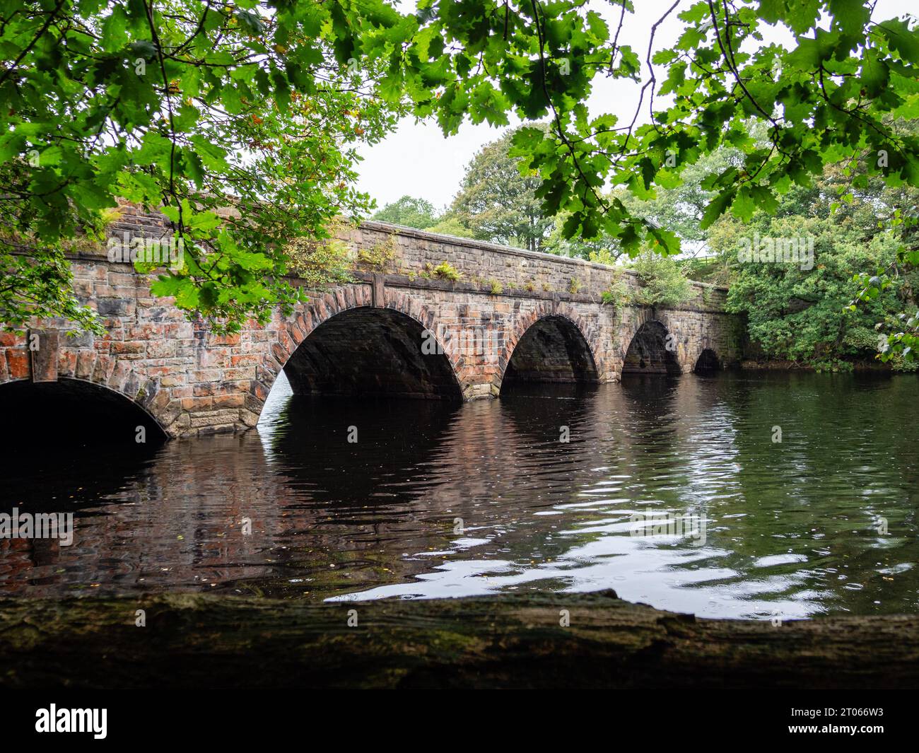 vecchio ponte costruito in pietra che abbraccia le acque buie del fiume lento e fluente con alberi a strapiombo, senza corpo Foto Stock