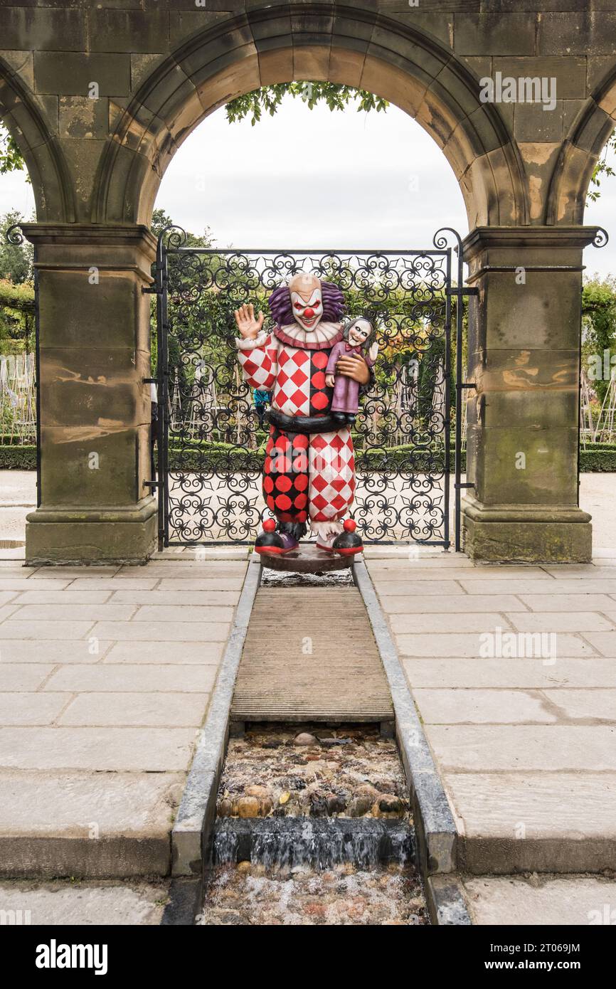 Divertente personaggio clown in mostra agli Alnwick Gardens nel Northumberland, vicino ad arco recintato e all'acqua. Foto Stock