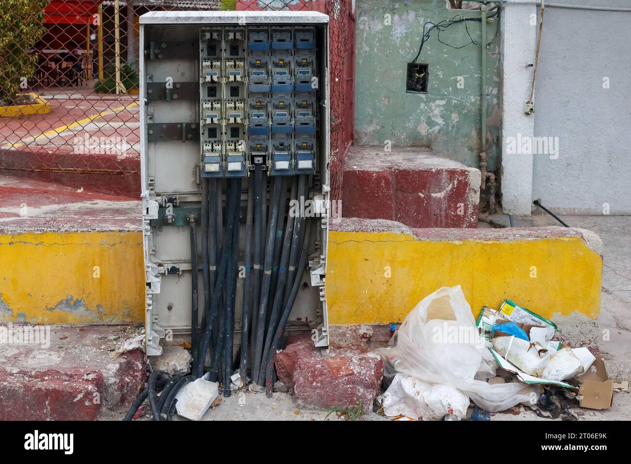 Una discarica vicino a una cassetta elettrica in un marciapiede della città. Il cortile sul retro di un ristorante con patio sullo sfondo. Foto Stock