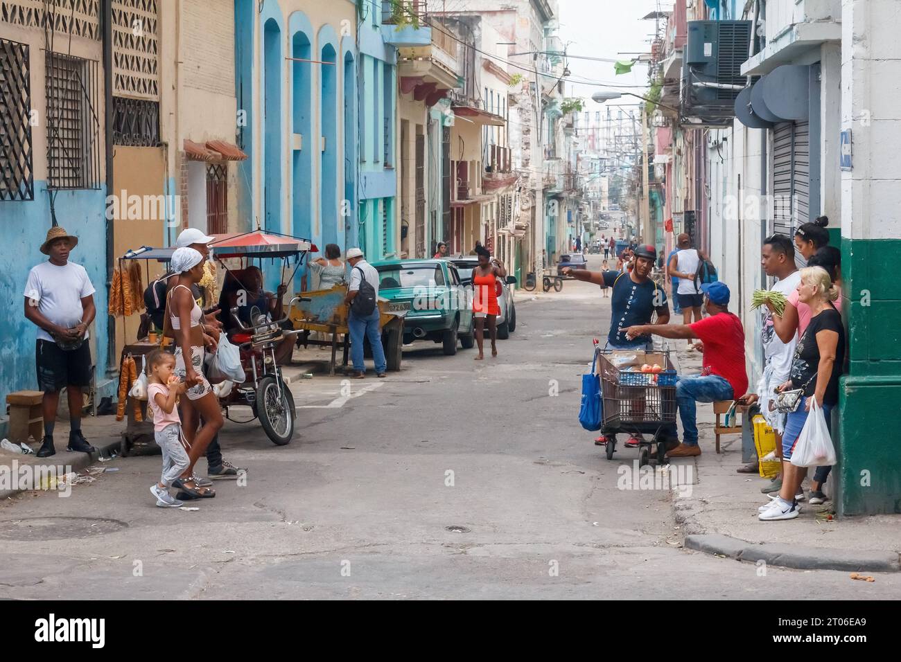 Un cubano vende prodotti alimentari con un piccolo carrello in un angolo della città. Lo stile di vita urbano di altre persone è mostrato nella scena della strada. Foto Stock