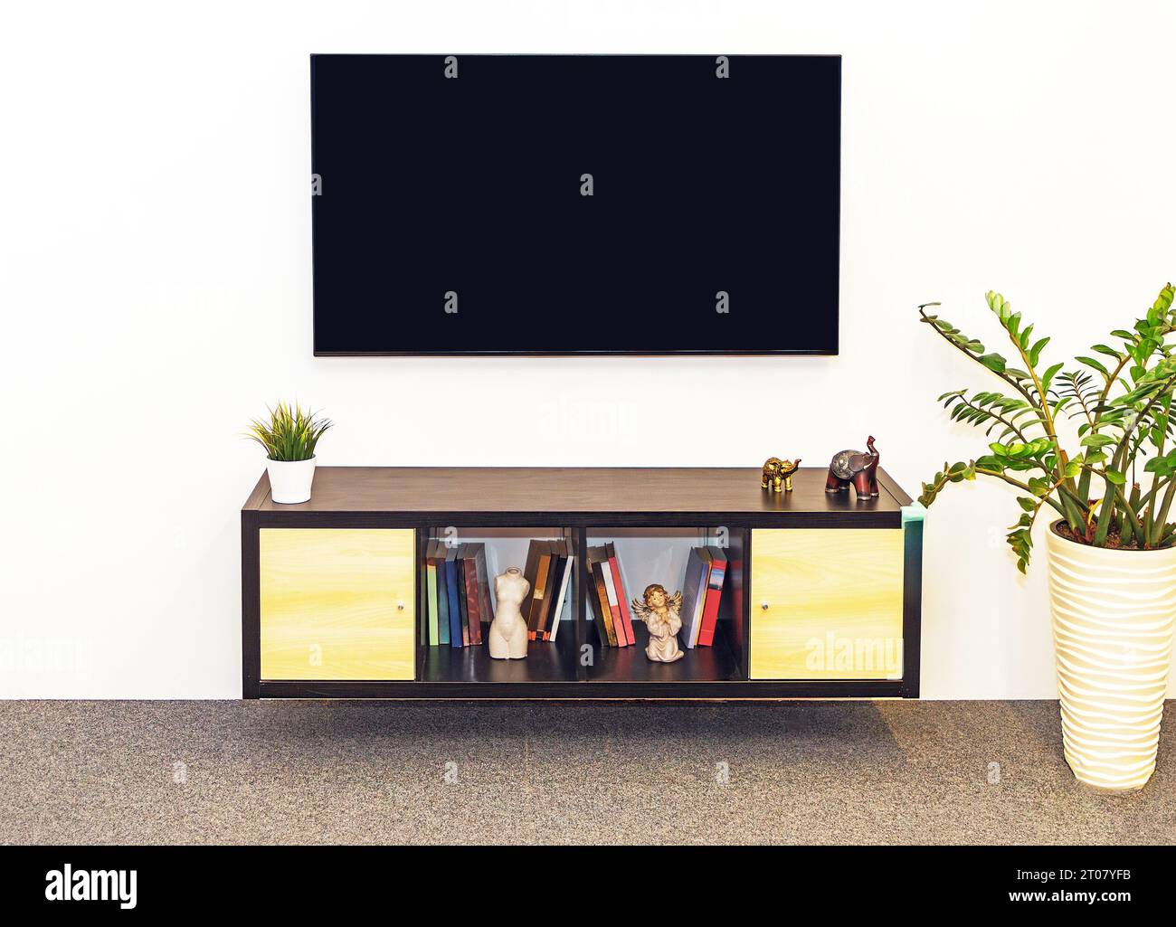 Grande schermo TV appeso a una parete in un interno di casa con armadietto in legno pieno di libri Foto Stock