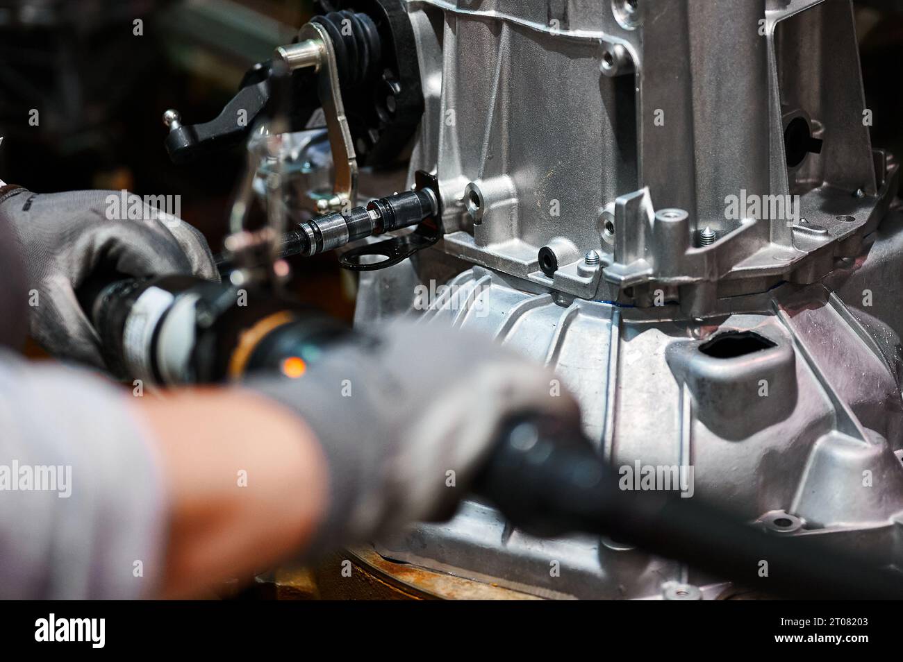 L'operatore collega i dettagli della scatola ingranaggi del motore dell'auto sul trasportatore dell'officina Foto Stock