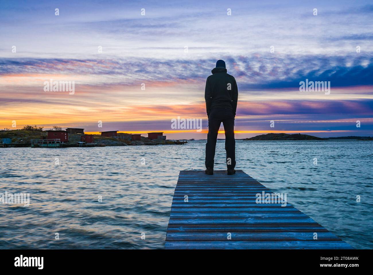 Una persona in piedi su un molo al tramonto, ammirando lo splendido oceano. Foto Stock