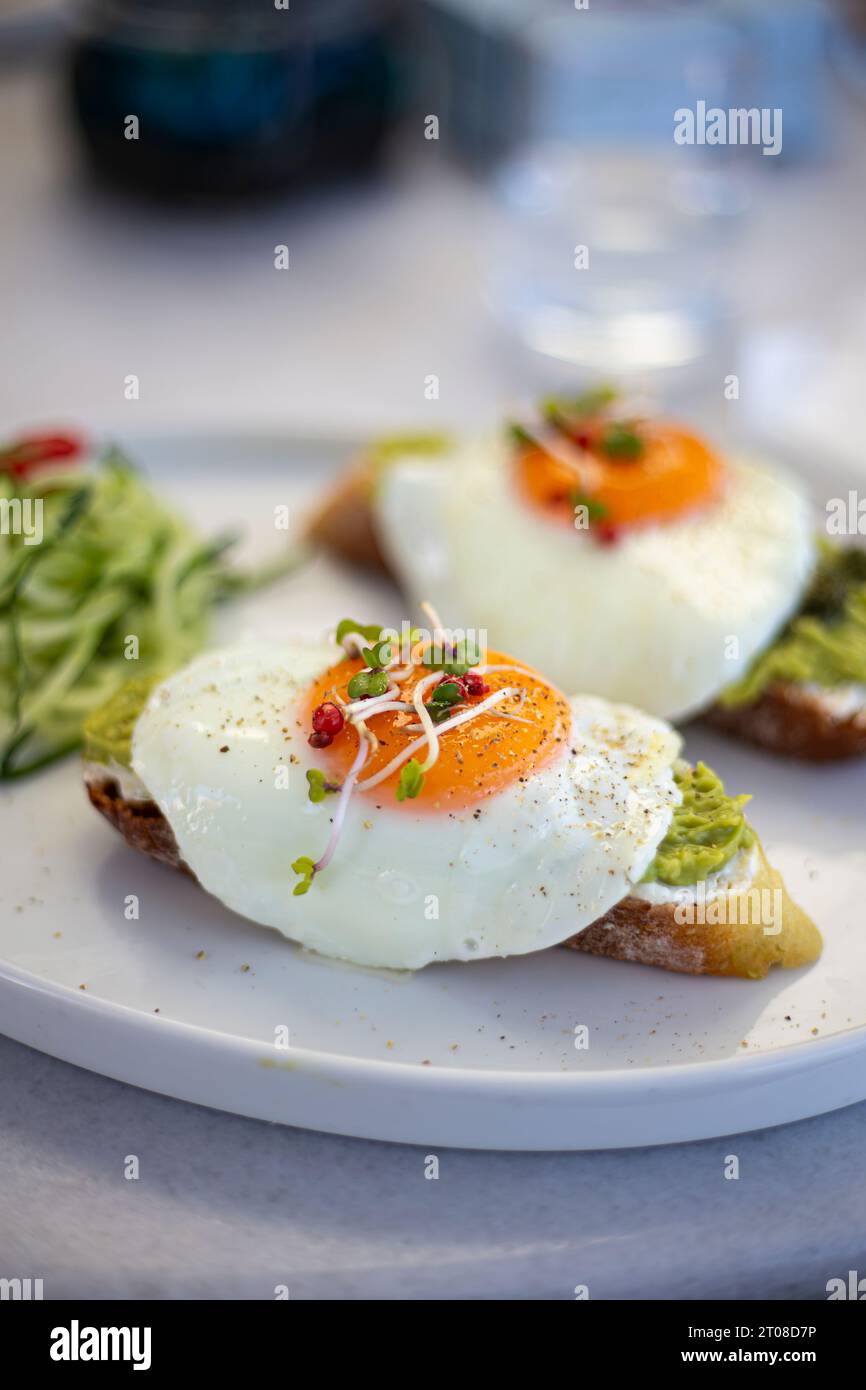 Gustosi e bellissime uova alla benedict fritte servite con toast all'avocado per colazione da vicino Foto Stock