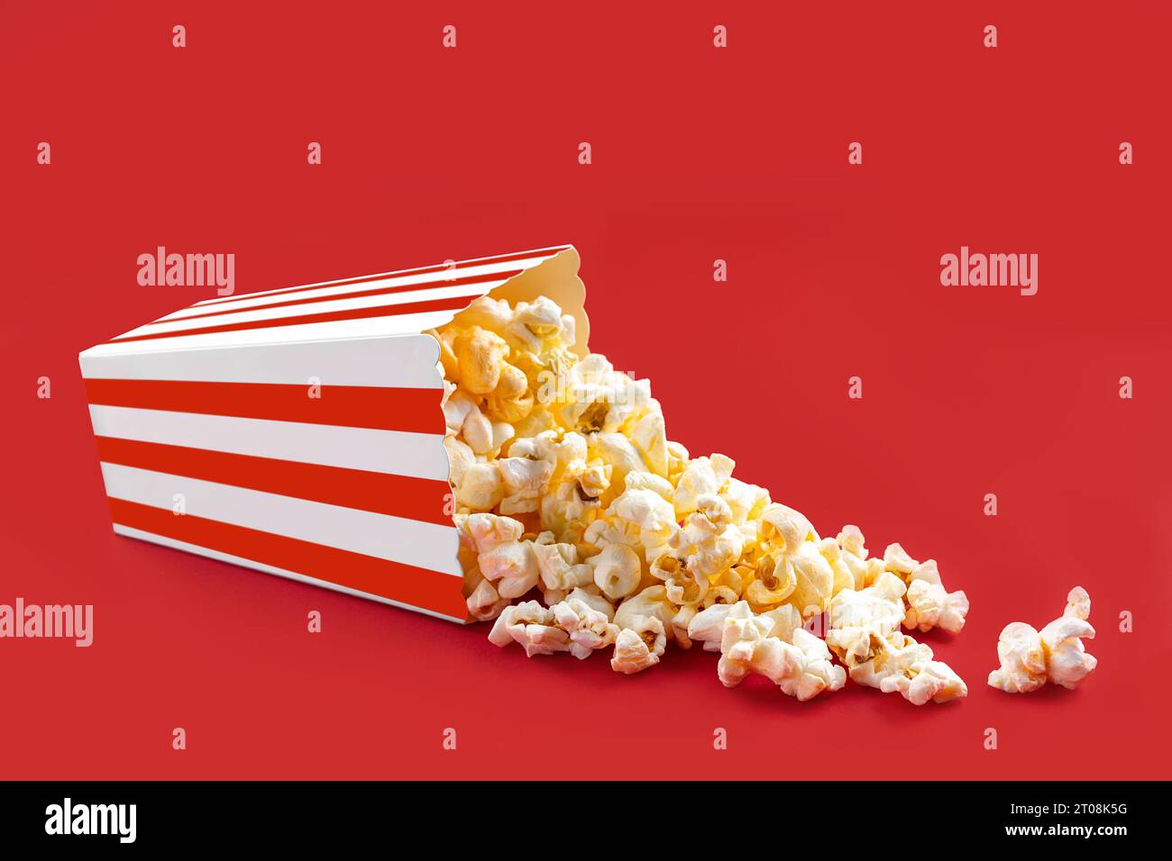 Gustosi popcorn al formaggio che cadono da una scatola di cartone a righe rosse o da un secchio, isolato su sfondo rosso. Dispersione di semi di popcorn. Fast food, snack. Mo Foto Stock