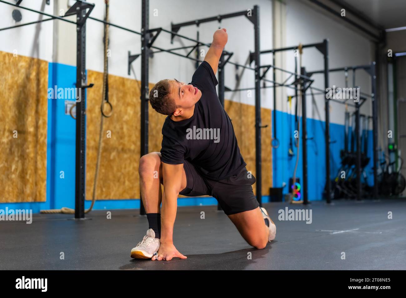 Uomo con un braccio amputato che si allunga da solo in una palestra di cross training Foto Stock