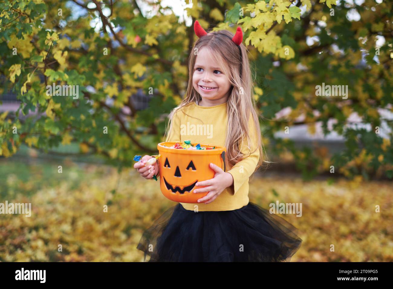 Gioiosa ragazza in costume da Halloween con un secchio di caramelle in autunno. trick o dolcetto. Foto Stock