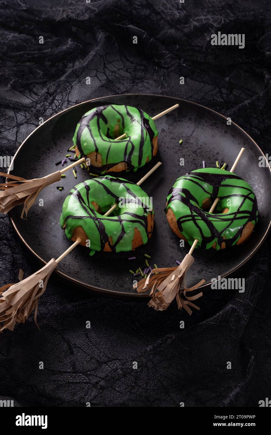 Ciambella di Halloween con glassa verde e scopa da strega. Scherzetto o scherzetto di Halloween. Foto Stock