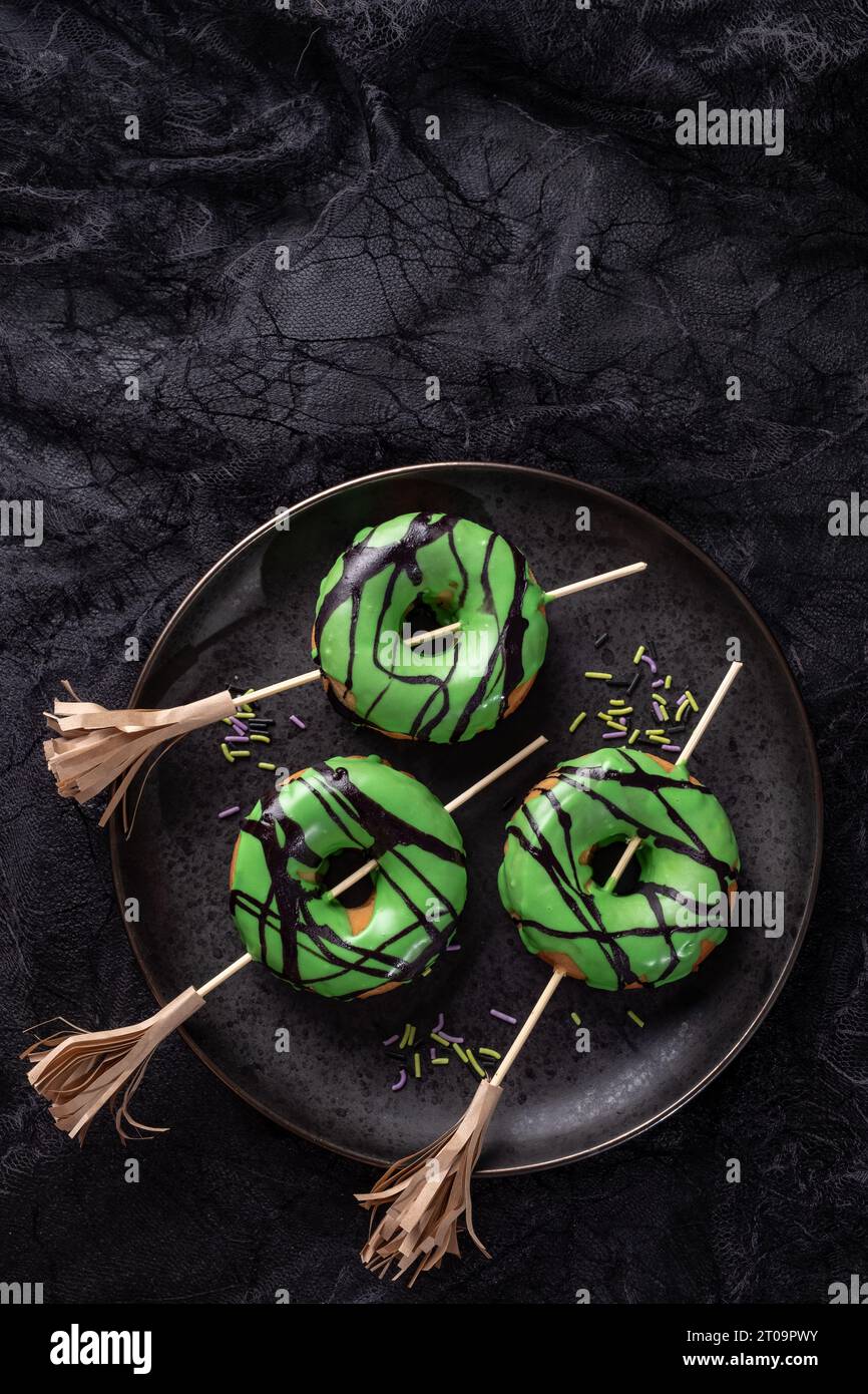 Ciambella di Halloween con glassa verde e scopa da strega. Scherzetto o scherzetto di Halloween. Foto Stock