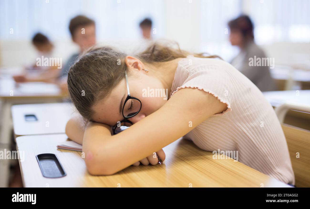 Una studentessa stanca e annoiata che dorme alla scrivania Foto Stock