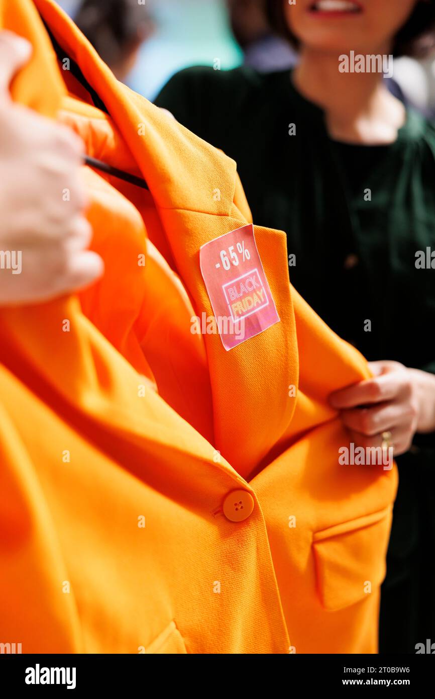 Persone che cadono nella follia dello shopping durante le vendite del Black Friday. Due clienti arrabbiati che lottano per il blazer arancione nel grande magazzino di abbigliamento, impazziscono durante le vendite stagionali Foto Stock