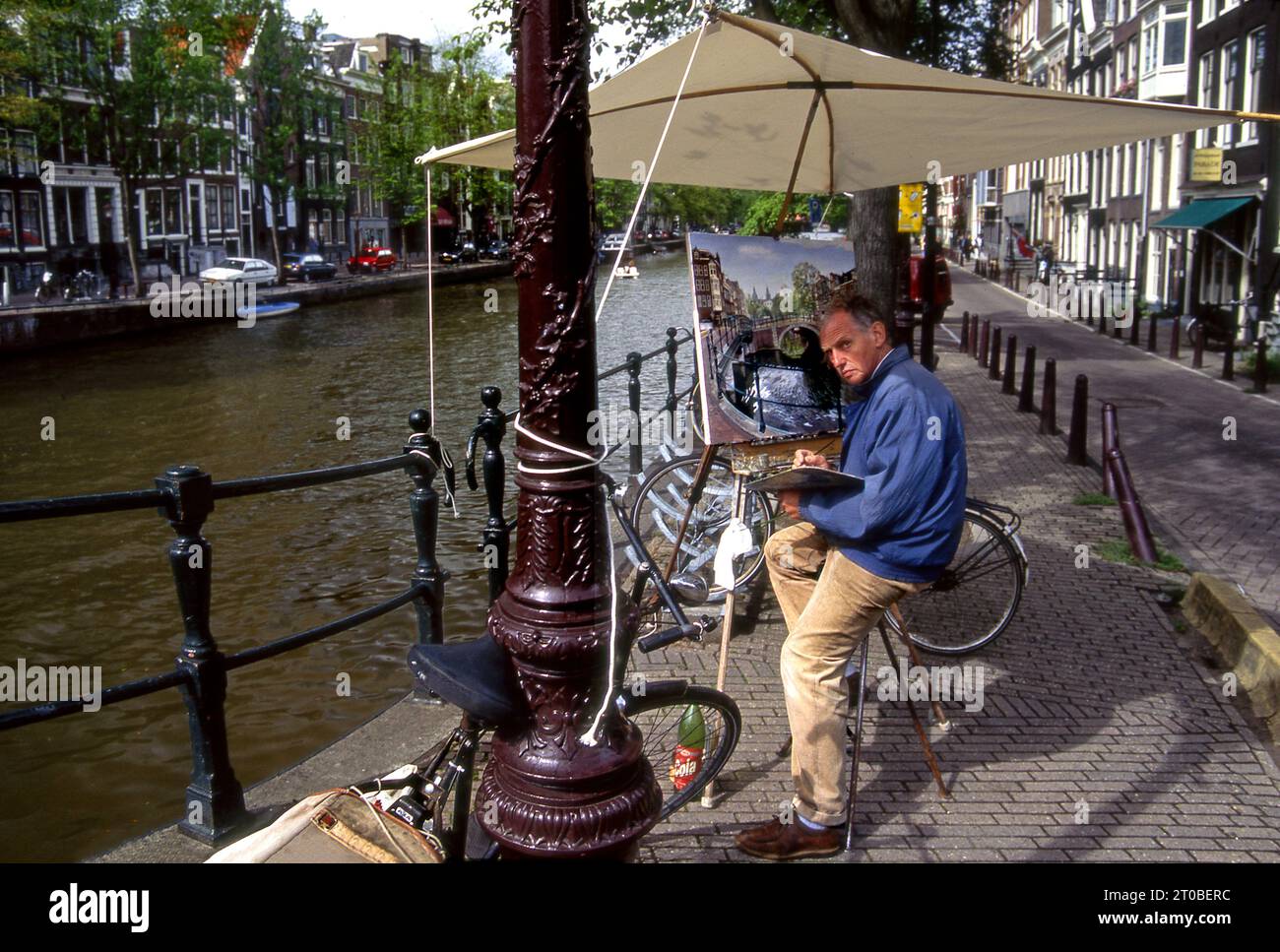 Artista con tela su cavalletto e ombrello che realizza un dipinto lungo i canali di Amsterdam, Olanda Foto Stock