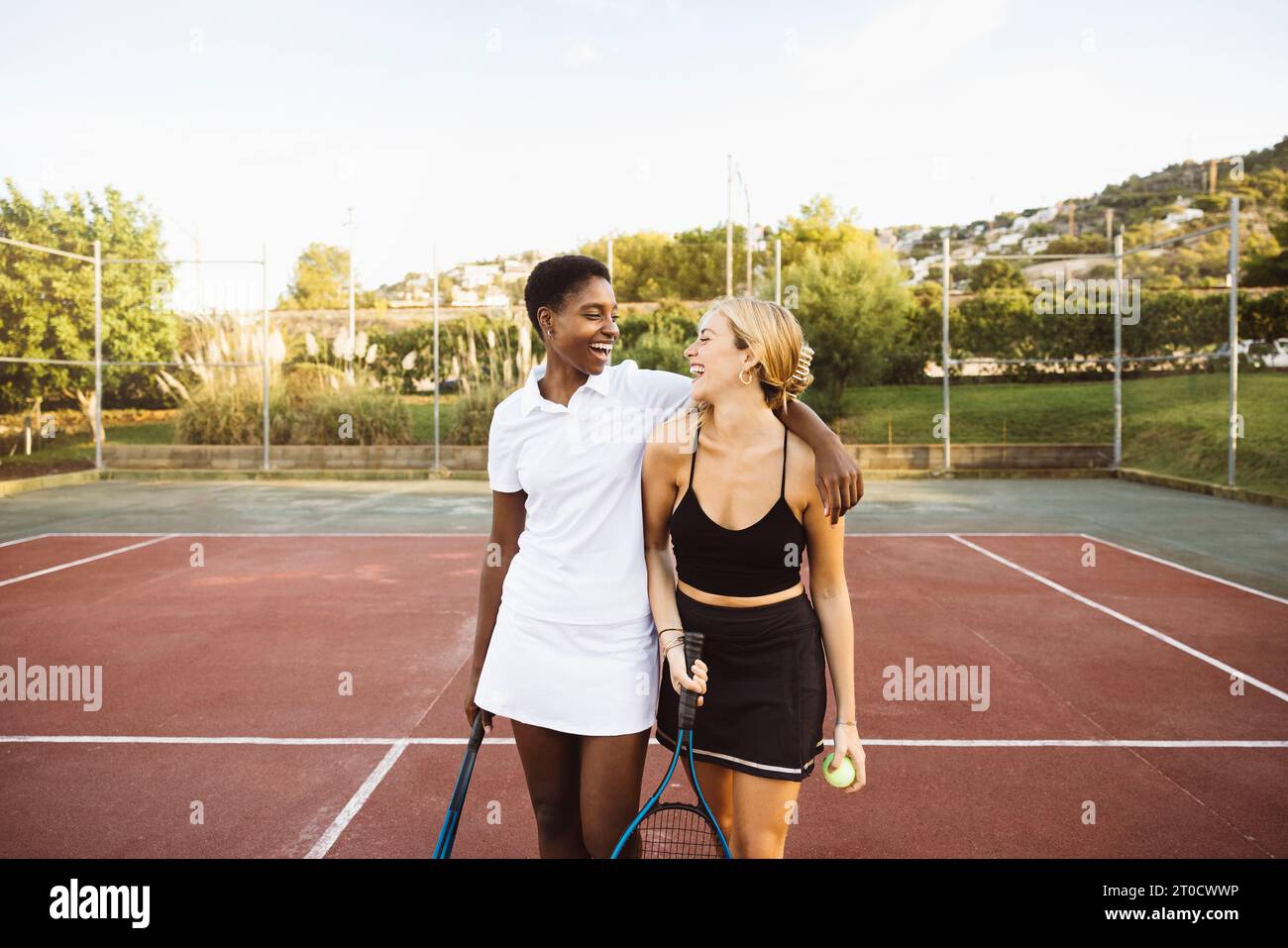 Due giovani belle donne sorridenti su un campo da tennis dopo aver giocato una partita di tennis amatoriale in una giornata di sole. Foto Stock