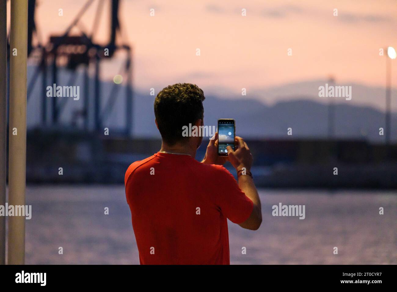 promenade, Malaga, Sunrise, uomo che scatta foto con il cellulare sulla schiena, t-shirt rossa Málaga, Sunrise, uomo che scatta foto con il suo cellulare sul suo b Foto Stock