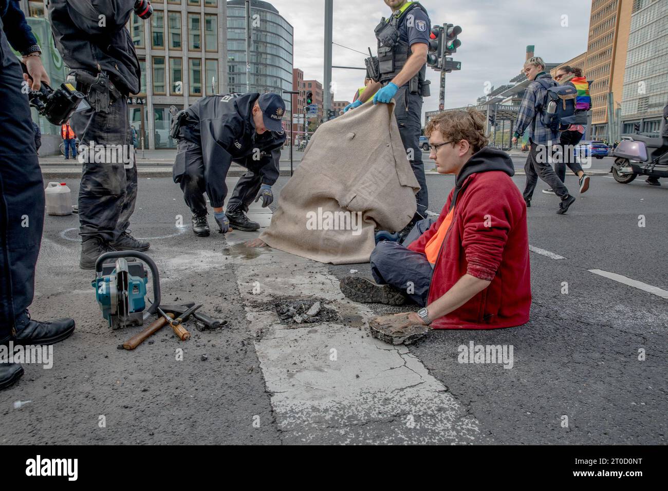 Berlino, Germania. 6 ottobre 2023. Gli attivisti climatici del gruppo ''Letzte Generation'' (Last Generation) nella disobbedienza civile si sono incollati e cementati sulla strada a Potsdamer Platz a Berlino il 6 ottobre 2023, causando significative interruzioni del traffico. La ''generazione Letzte'', nota per i loro metodi di protesta non convenzionali, mira a spingere i governi ad aderire agli obiettivi dell'accordo di Parigi, principalmente l'obiettivo a 1,5 gradi. La polizia, nel tentativo di liberare gli attivisti dalle strade, ha fatto ricorso all'olio da cucina e alle seghe circolari. Anche le conseguenze giuridiche hanno seguito il loro prot Foto Stock