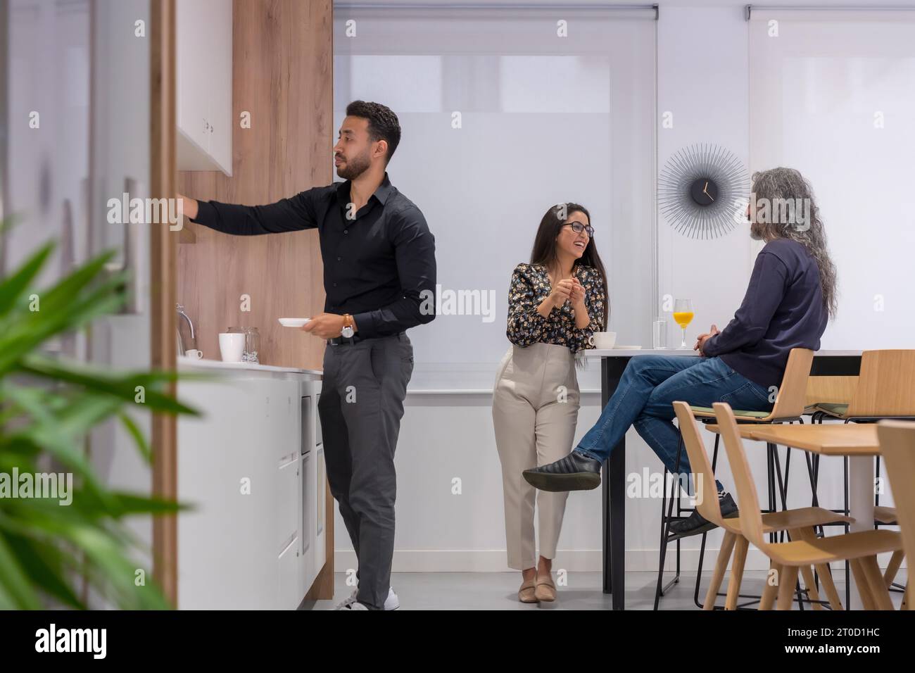 Tre colleghi che parlano si sono rilassati nella cucina di uno spazio di co-working durante una pausa caffè Foto Stock