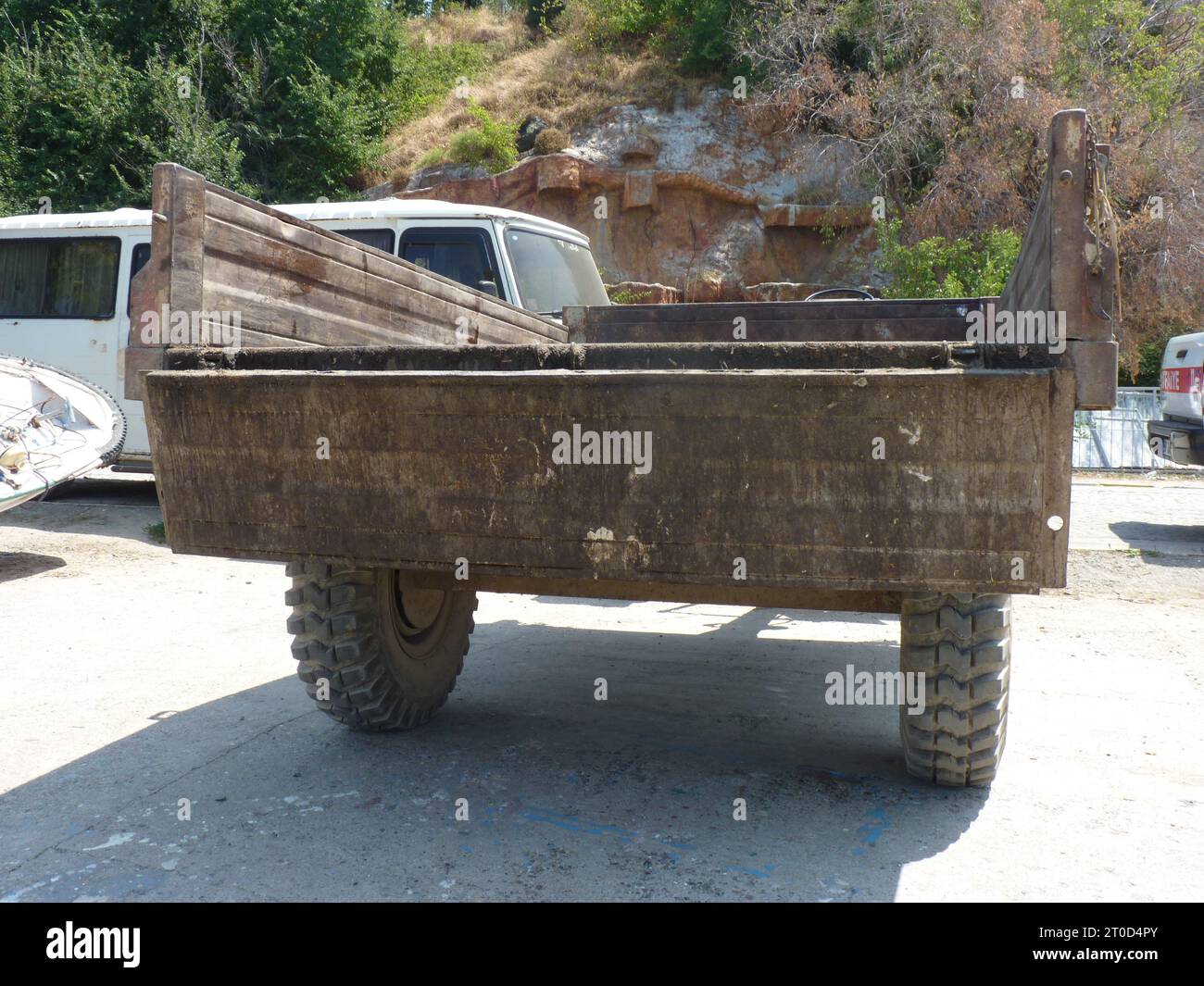 Carrello in legno arrugginito con letto piatto e pneumatici con battistrada in gomma su superficie in calcestruzzo in ambiente naturale Foto Stock