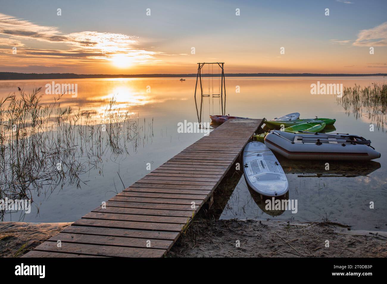 Vista panoramica sulla romantica alba sul Lago bianco con altalena in legno, molo e barche nella regione di Rivne, Ucraina. Foto Stock