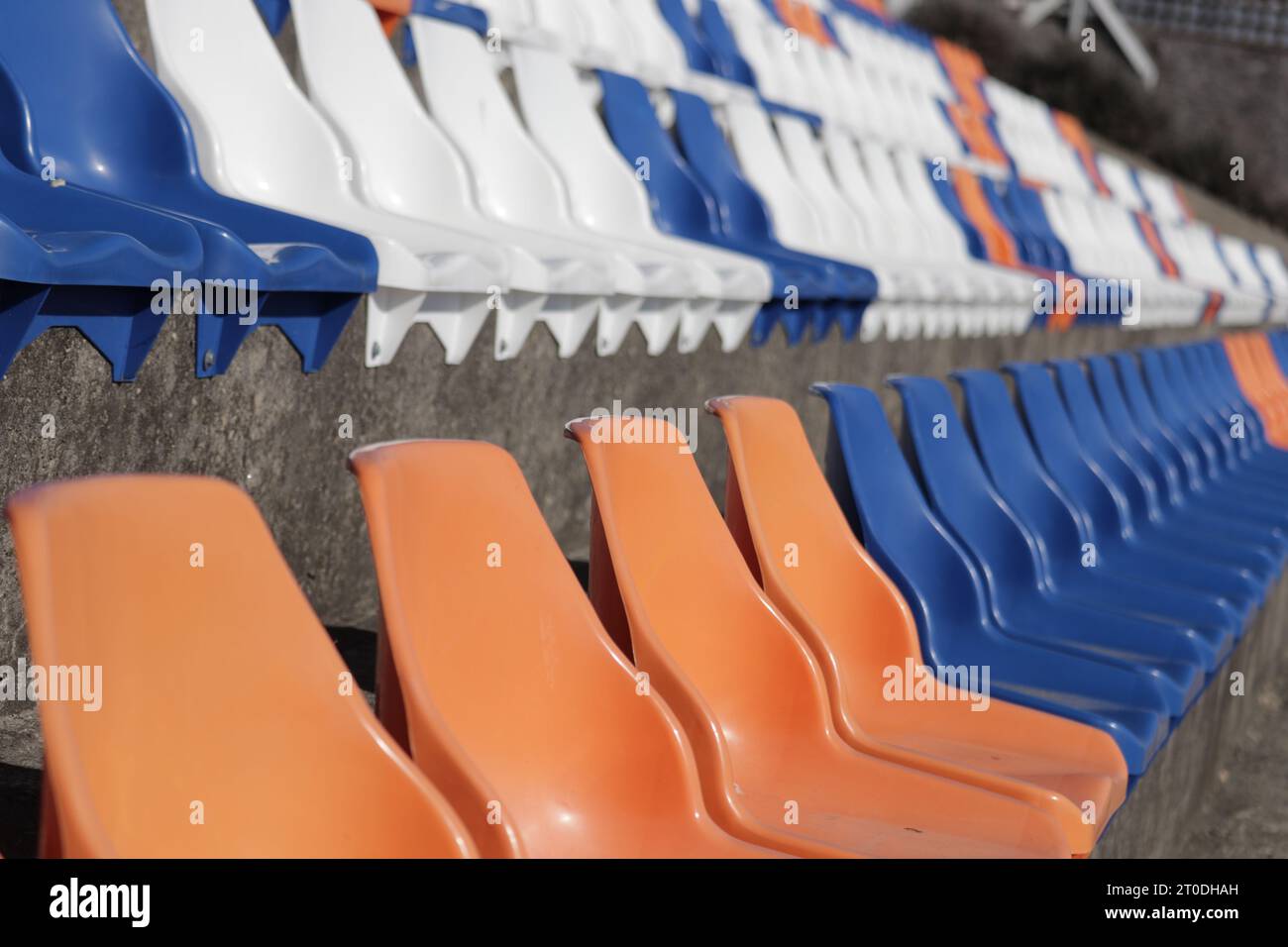 Una linea luminosa di sedie in plastica arancione rivestiva il terreno esterno, portando un'energia vibrante al cielo blu Foto Stock