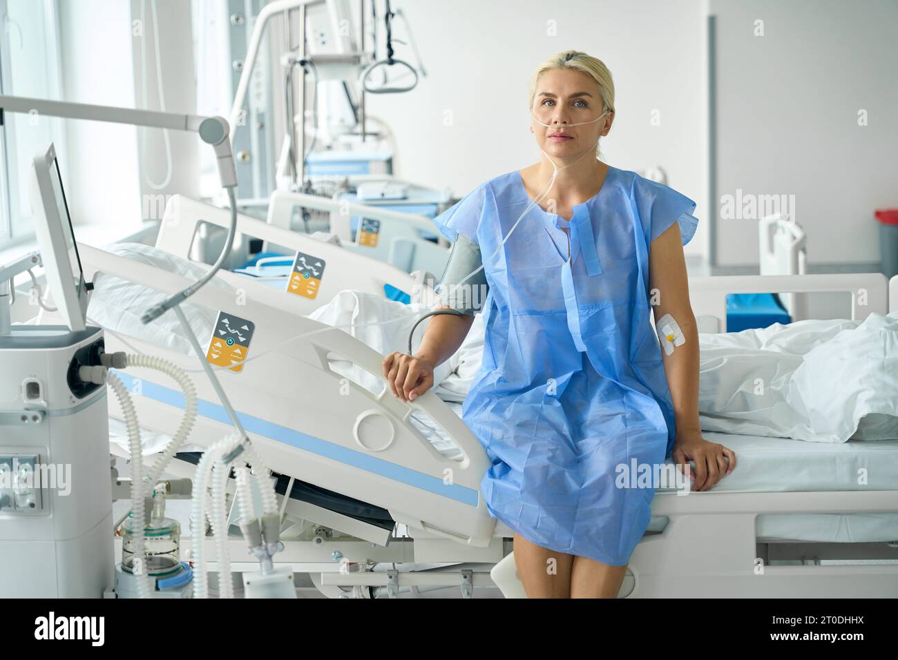 Lady in abito d'ospedale siede sul letto in unità di terapia intensiva Foto Stock