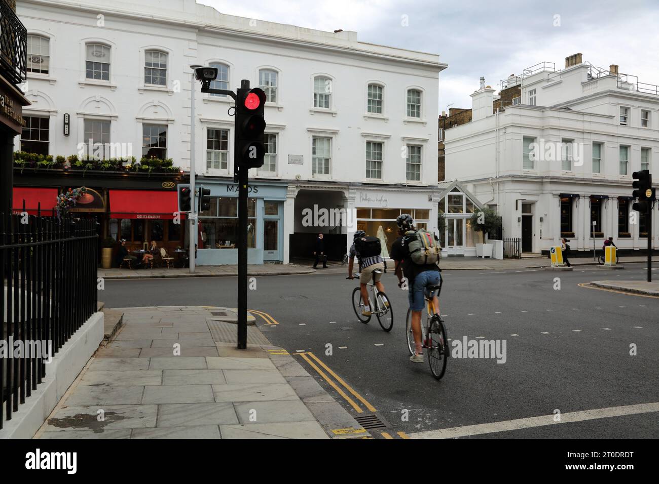 Ciclisti che corrono attraverso i semafori rossi su Sydney Street fino a Fulham Road Chelsea Londra Inghilterra Foto Stock