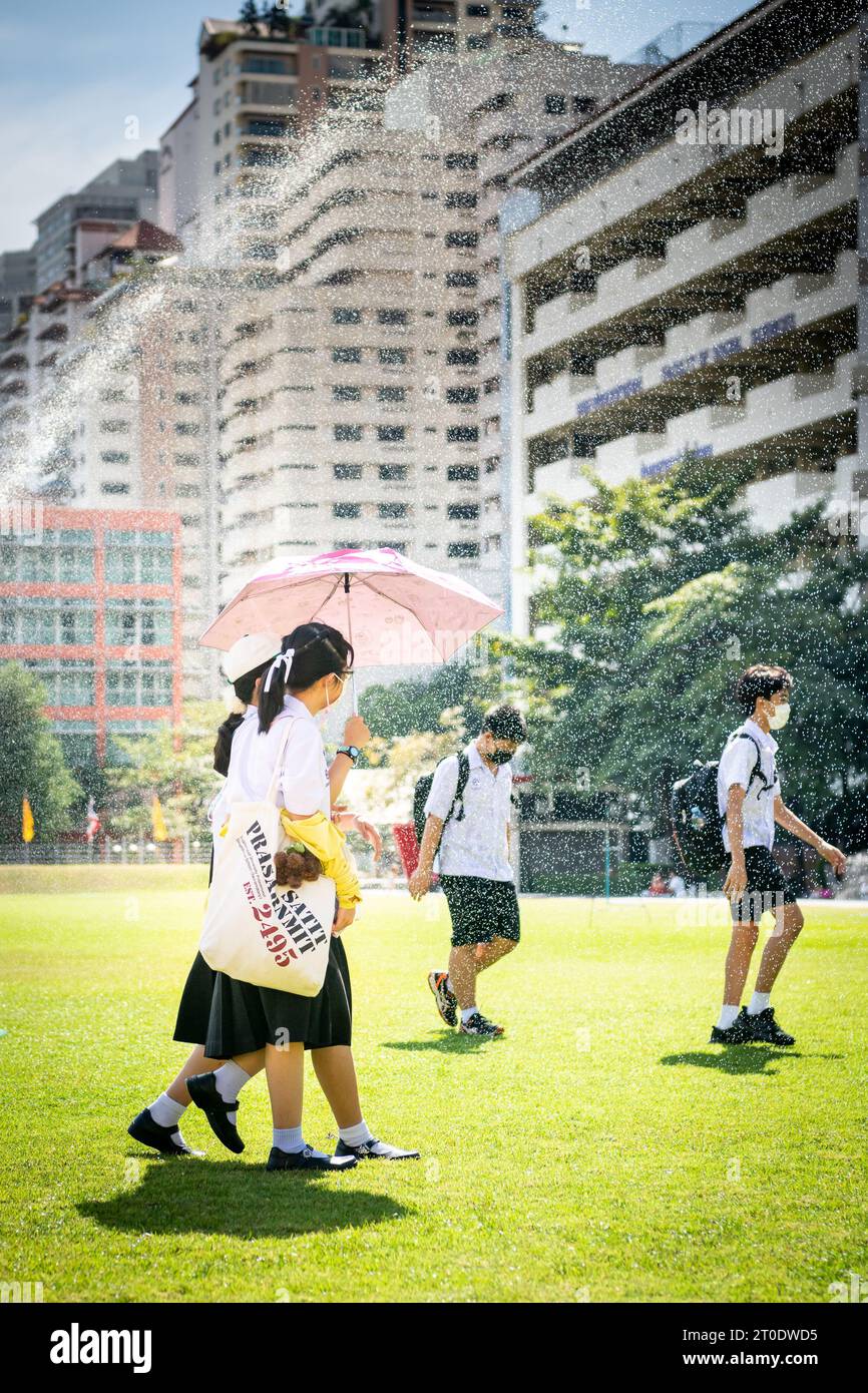 Gli studenti universitari thailandesi vagano attraverso il prato principale dell'Università Srinakharinwirot di Bangkok, Thailandia, e si bagnano dagli irrigatori da giardino. Foto Stock