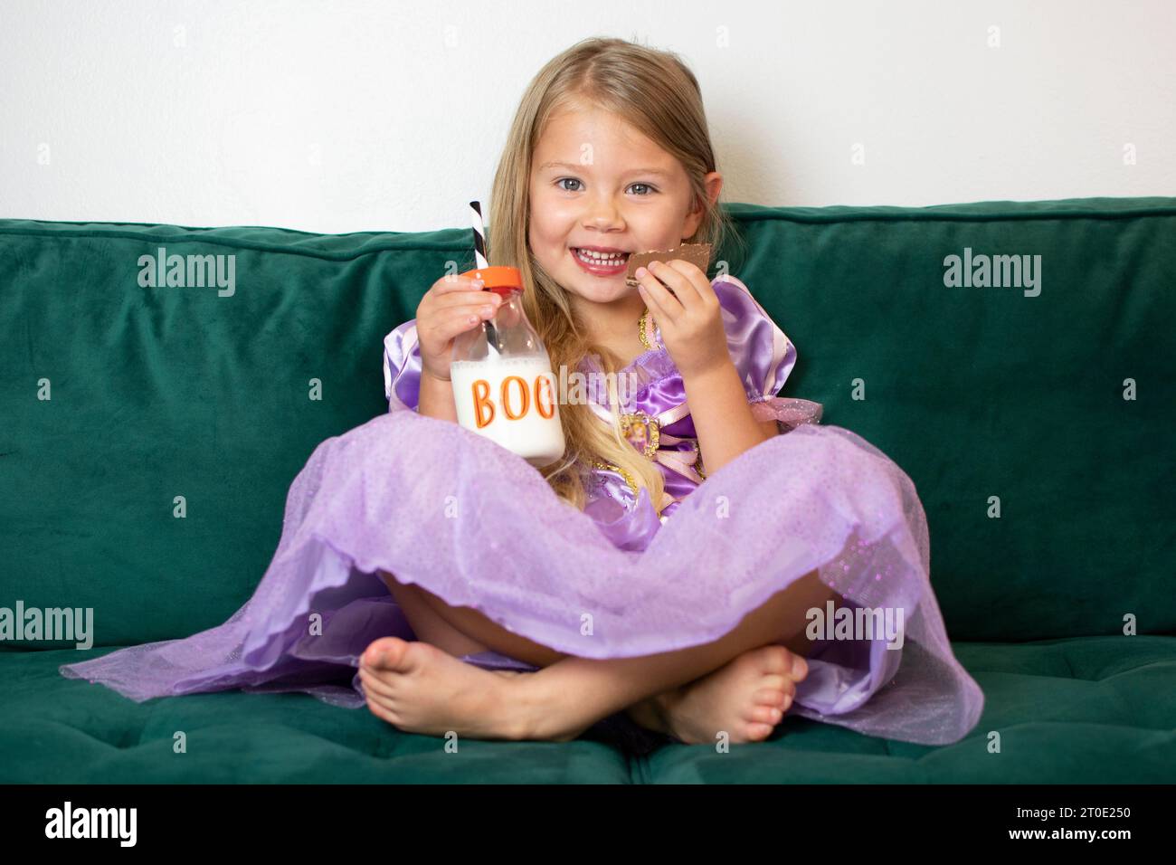 La graziosa bambina caucasica sta mangiando biscotti in costume di Halloween. Ragazza con vestito viola. Concetto bambini e Halloween Foto Stock