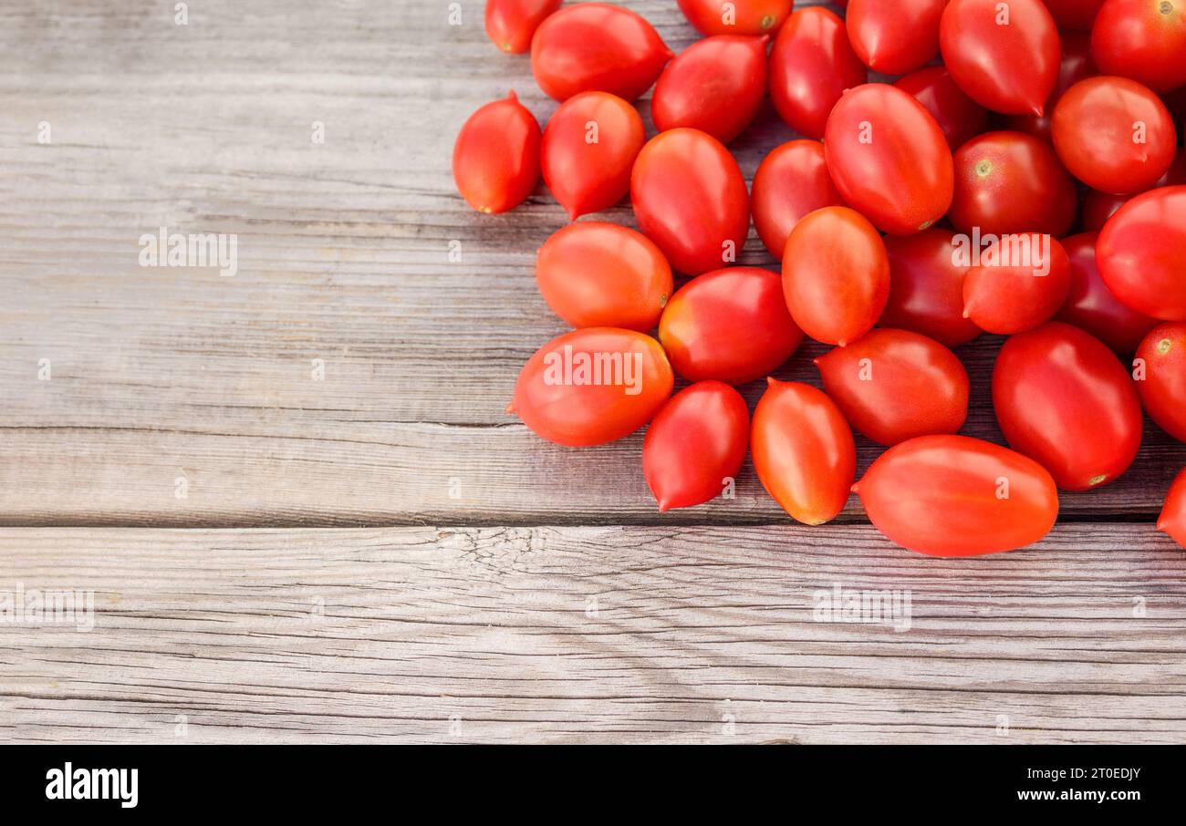 Pomodori ciliegini maturi su fondo di legno. Vista dall'alto dei pomodori a bacca rossa appena raccolti su tavola di legno. Pila casuale di pomodori zuccherati coltivati in Foto Stock