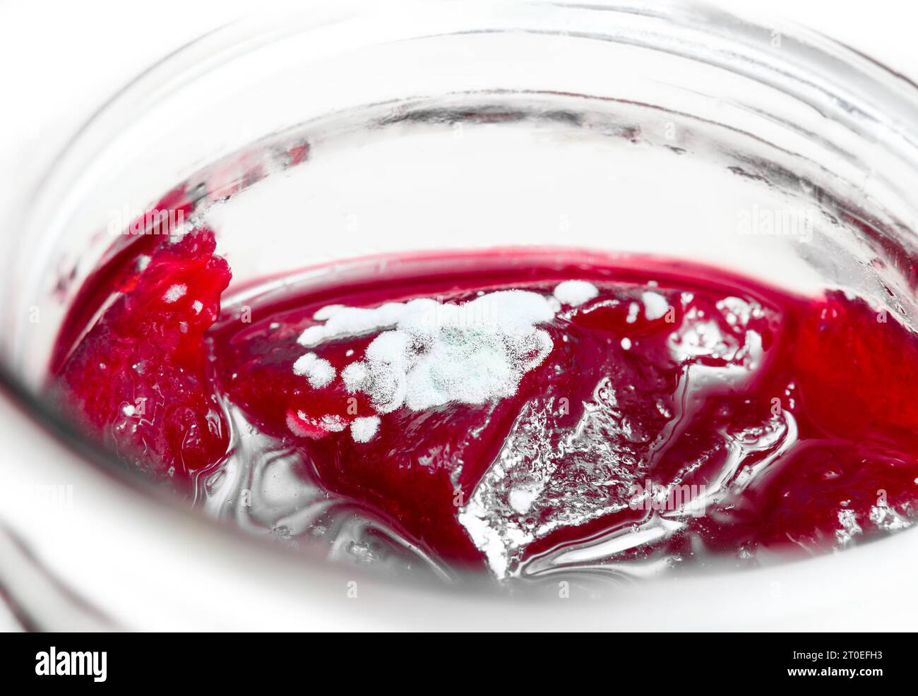 Marmellata di muffa in vaso, prospettiva. Marmellata di frutti di bosco rossi brillanti con spore bianche sfocate sulla parte superiore del barattolo mason. Concetto per la sicurezza alimentare, evitare di raschiare un Foto Stock
