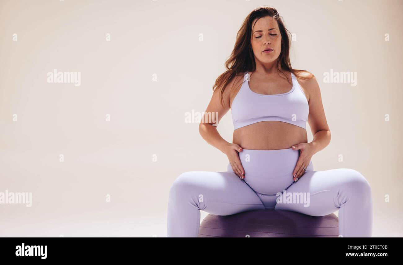 una donna incinta nel suo terzo trimestre pratica yoga prenatale su una palla di esercizio in un tranquillo studio. Si concentra su respirazione, flessibilità e stren Foto Stock