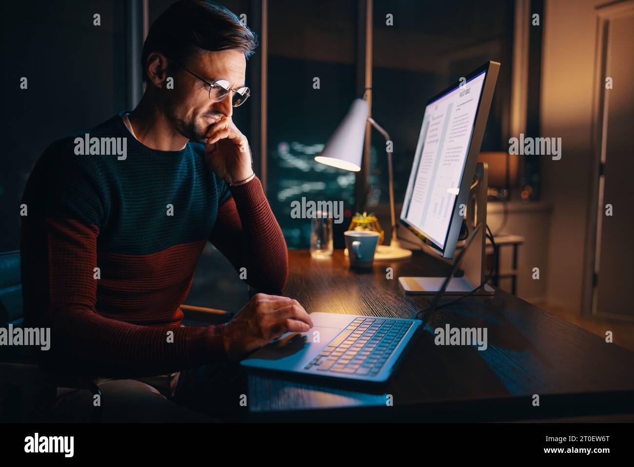 Un giovane imprenditore concentrato lavora fino a tardi nel suo ufficio, impegnato in una riunione online. E' determinato, penoso e devoto ai suoi affari. Foto Stock
