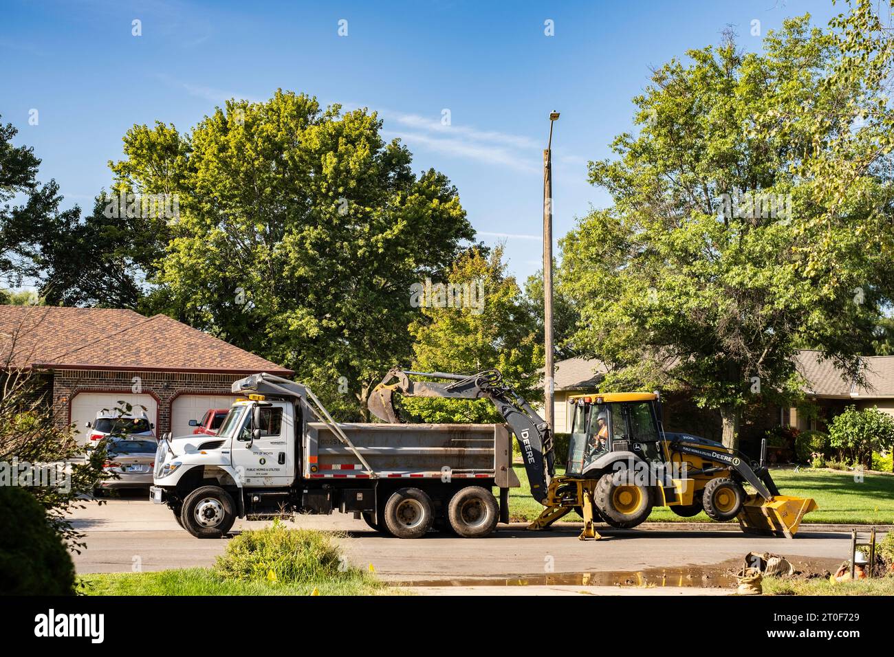 Un dipendente del dipartimento idrico di Wichita, Kansas, scava una linea d'acqua con il retroescavatore John Deere con il bulldozer in un quartiere urbano. Wichita, Kansas, USA. Foto Stock