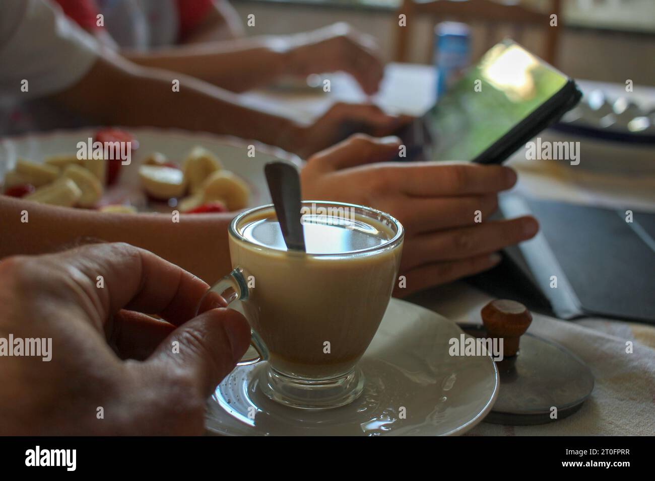 prendere un caffè bianco a casa con mio figlio che sta guardando il suo tablet mentre mangia un po' di frutta Foto Stock