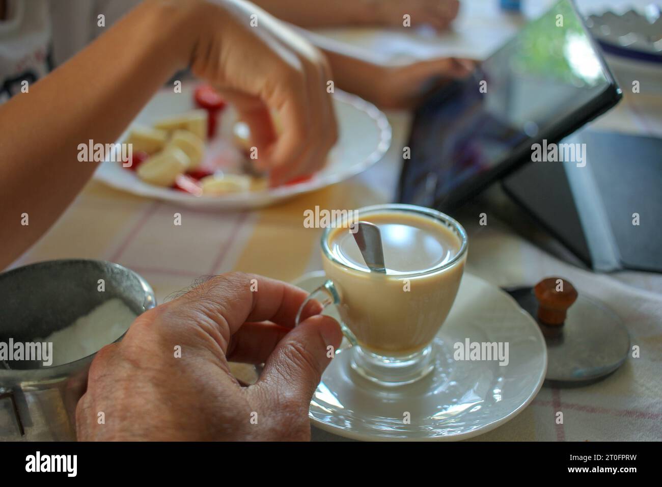 due persone che bevono un caffè e un po' di frutta e guardano un tablet in cucina Foto Stock