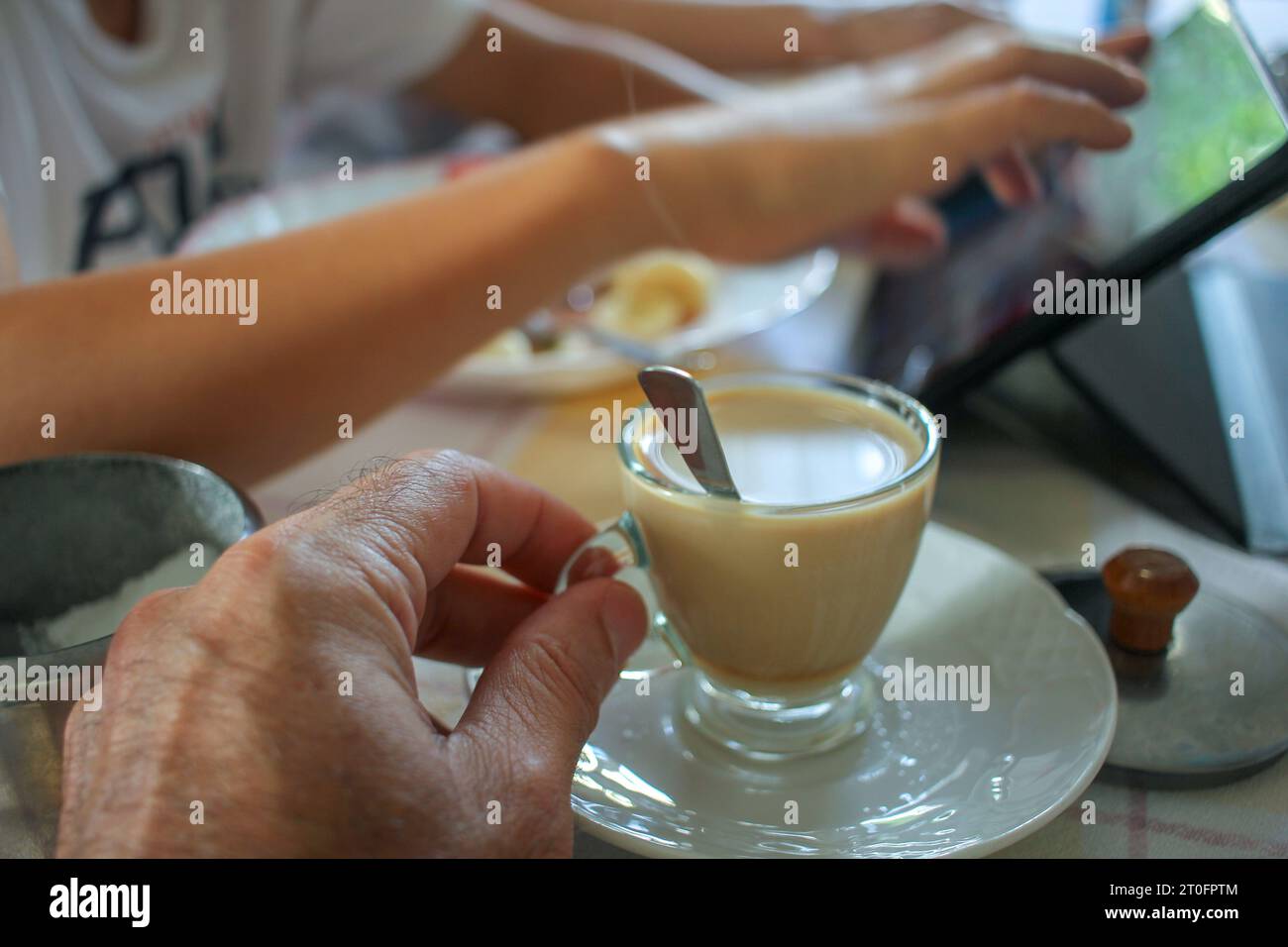 bevendo un caffè mentre mio figlio guarda il tablet e mangia un po' di frutta Foto Stock