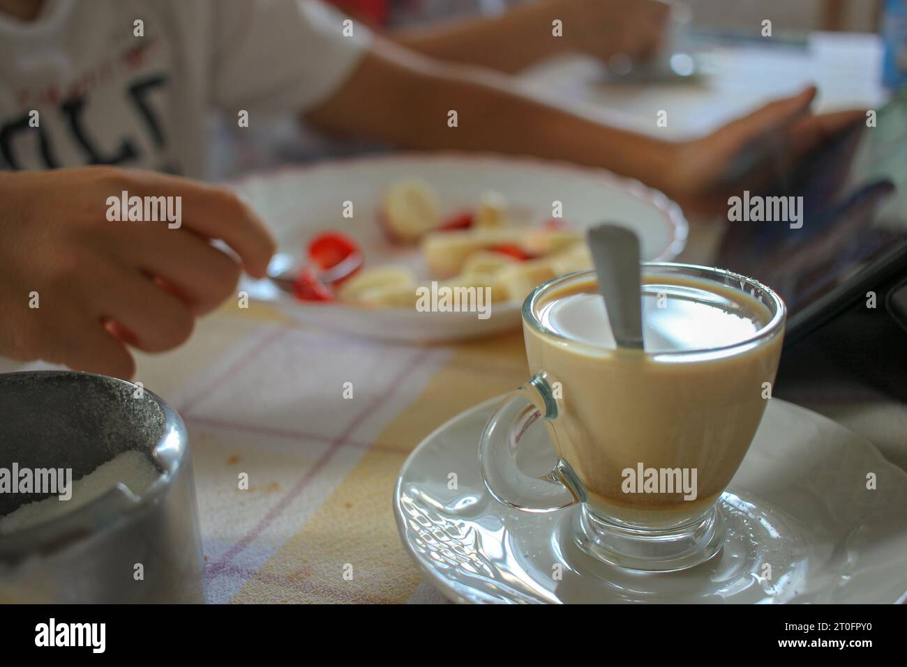 caffè con latte, zucchero, frutta e una tavoletta da guardare in cucina Foto Stock