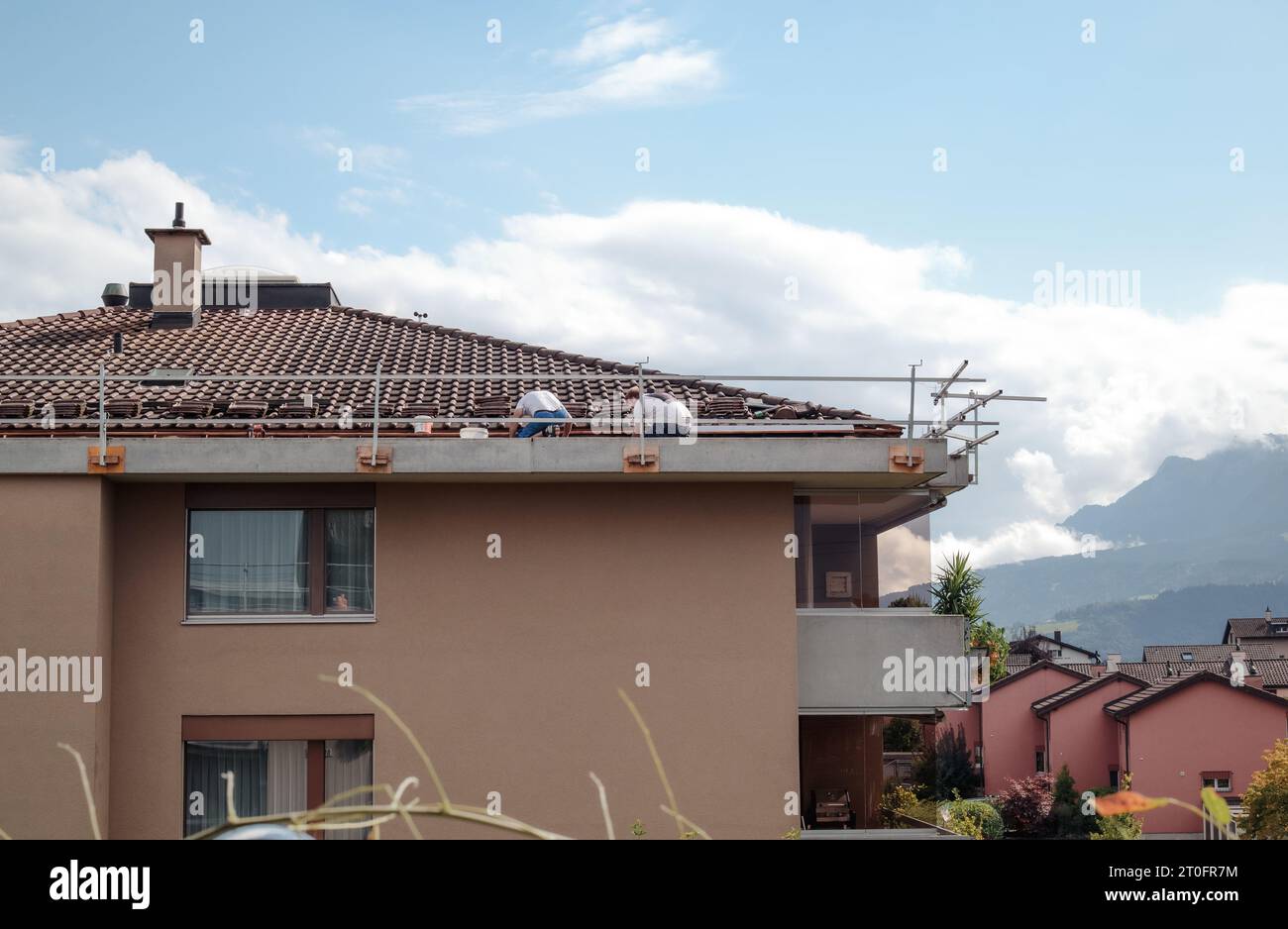 Appaltatori che lavorano sul tetto con piastrelle in ceramica su un edificio residenziale a 4 piani. I lavoratori hanno ringhiere di sicurezza, ma nessuna corda. Lavori di riparazione del tetto. Selettivo f Foto Stock