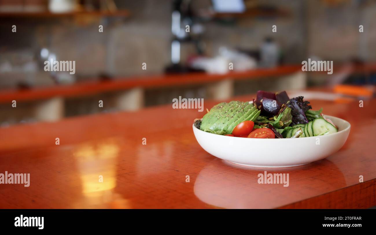 Grande ciotola per insalate sul tavolo con sfondo sfocato del ristorante. Pasti salutari o vegetariani. Insalata con varietà di verdure come l'avocad Foto Stock