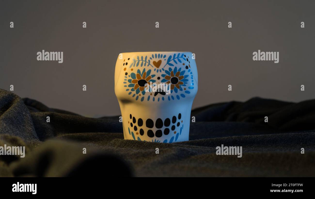 Una tazza dal volto teschio è un'audace dichiarazione di stile su un misterioso sfondo grigio-nero, che unisce estetica macabra e raffinatezza moderna Foto Stock