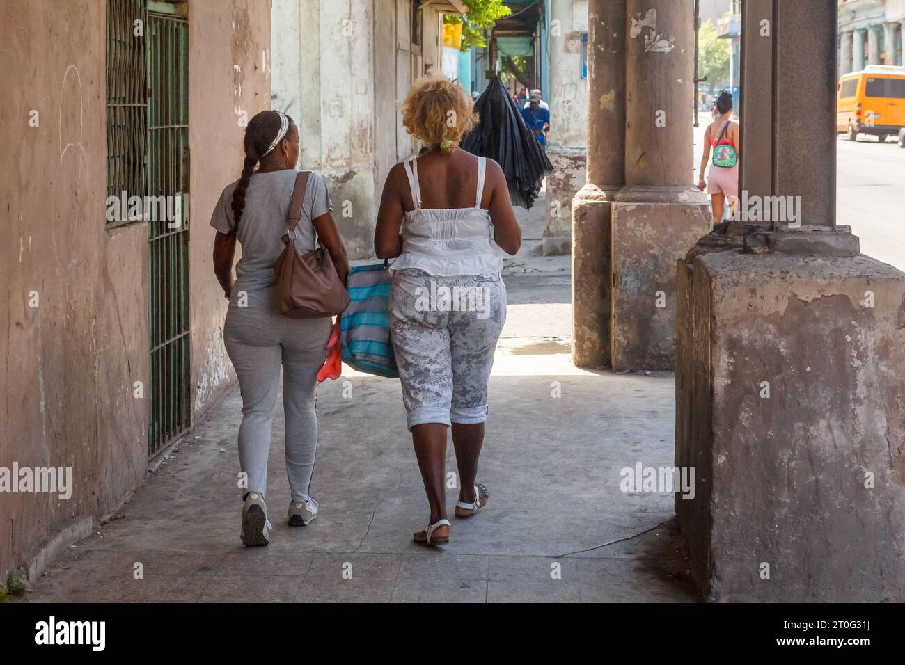 Due donne afro-caraibiche camminano in un portico di un edificio. Le pareti e il pavimento della struttura sembrano sporchi e intemprati. Foto Stock
